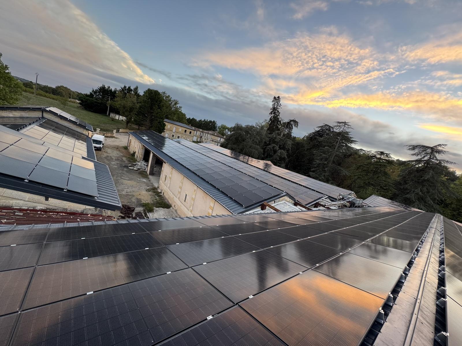 Plusieurs grandes toitures de bâtiments couvertes de panneaux photovoltaïques, au coucher du soleil